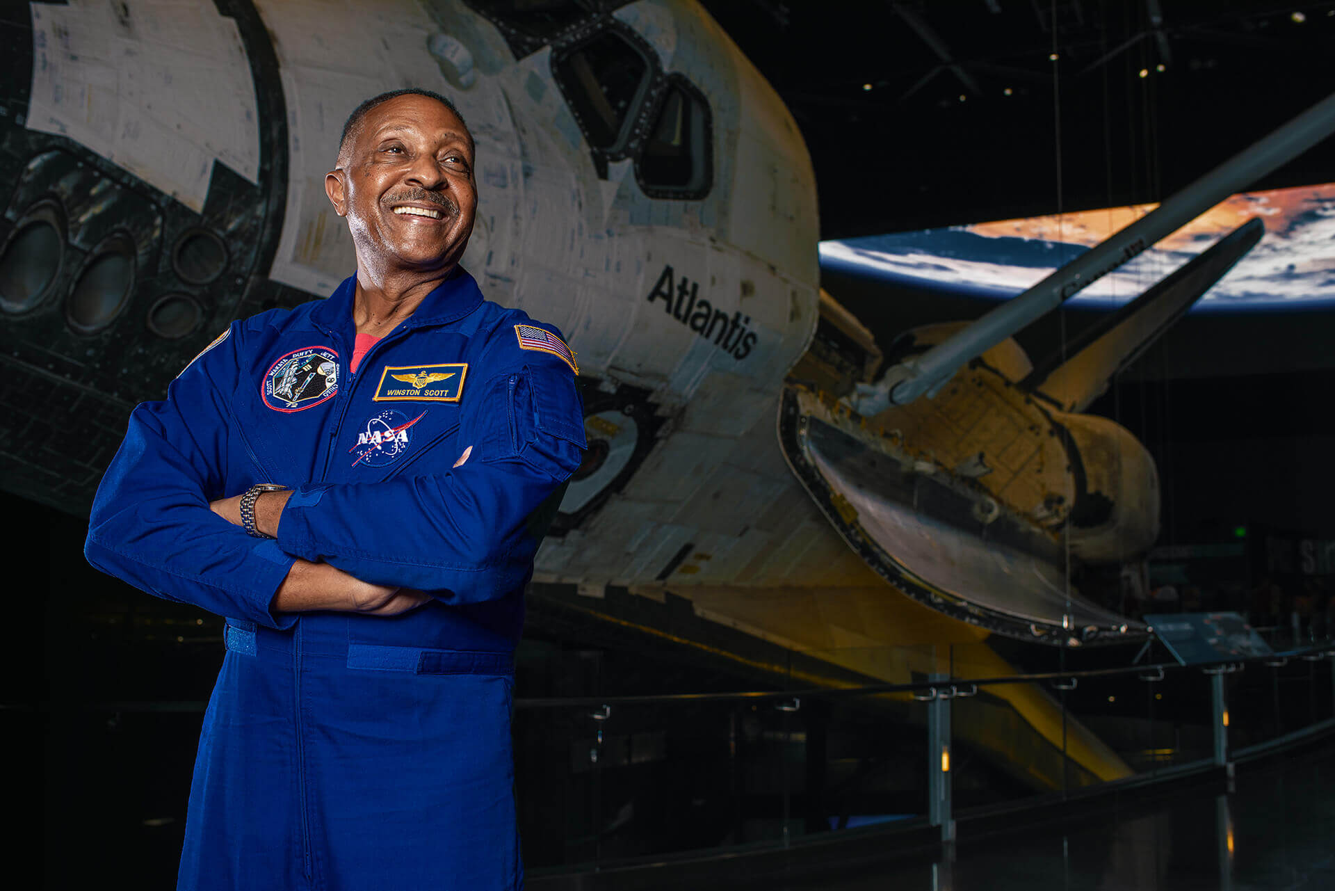 Winston Scott in a blue flight suit standing beside an aircraft.