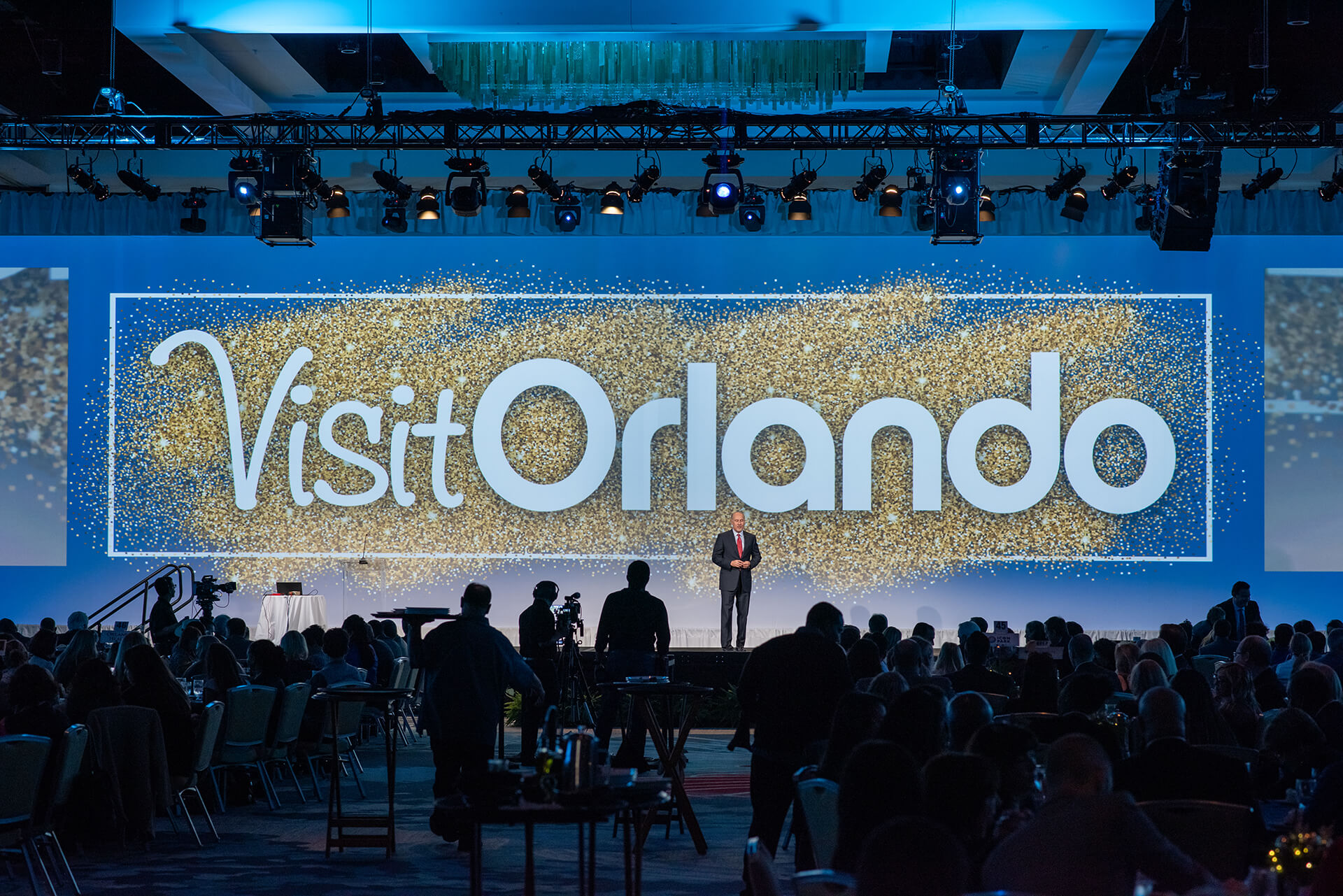 Conference audience facing a stage with a large Visit Orlando screen.