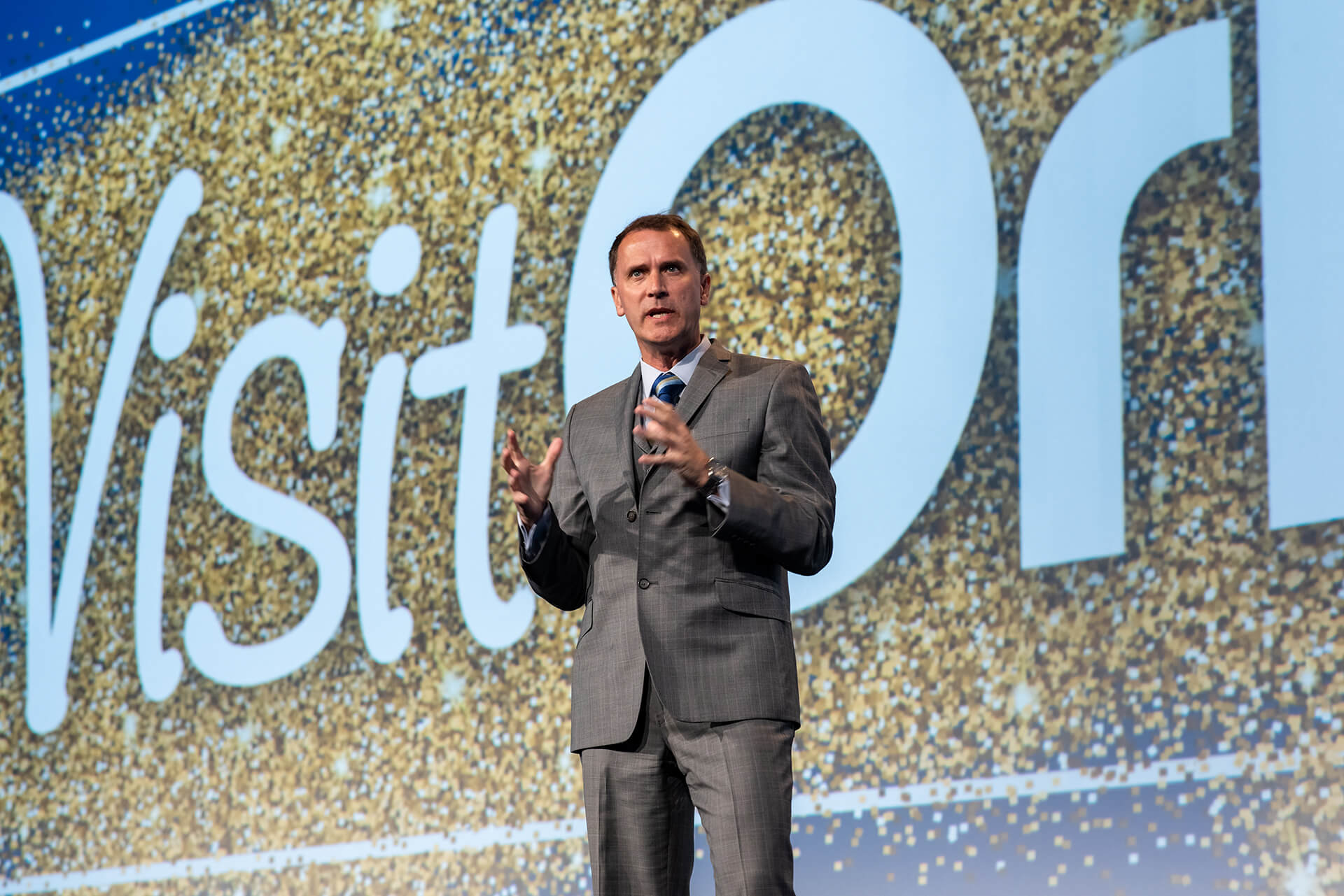 Speaker holding a microphone on a Visit Orlando conference stage.