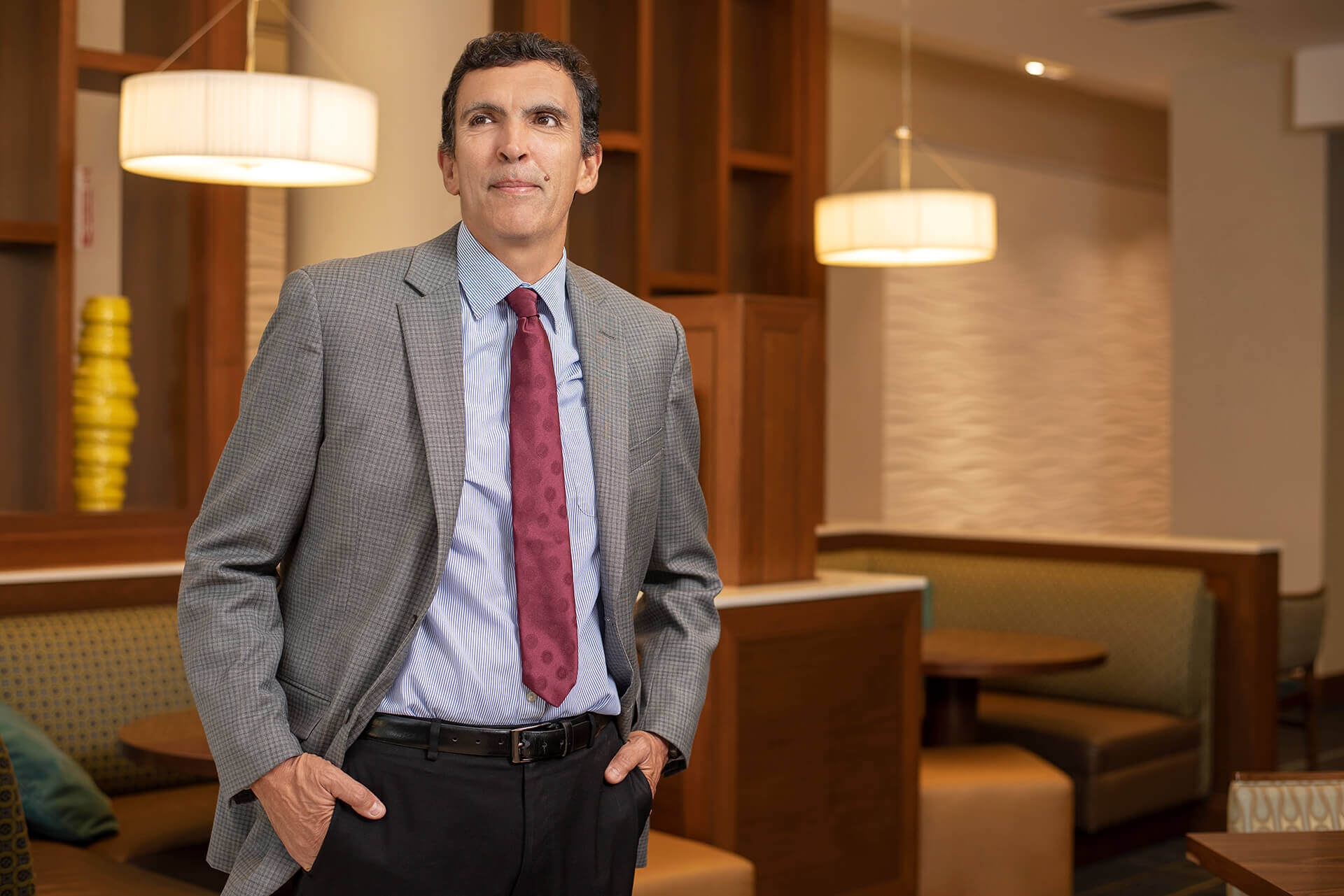 Man in a gray suit and red tie standing in a furnished lobby.