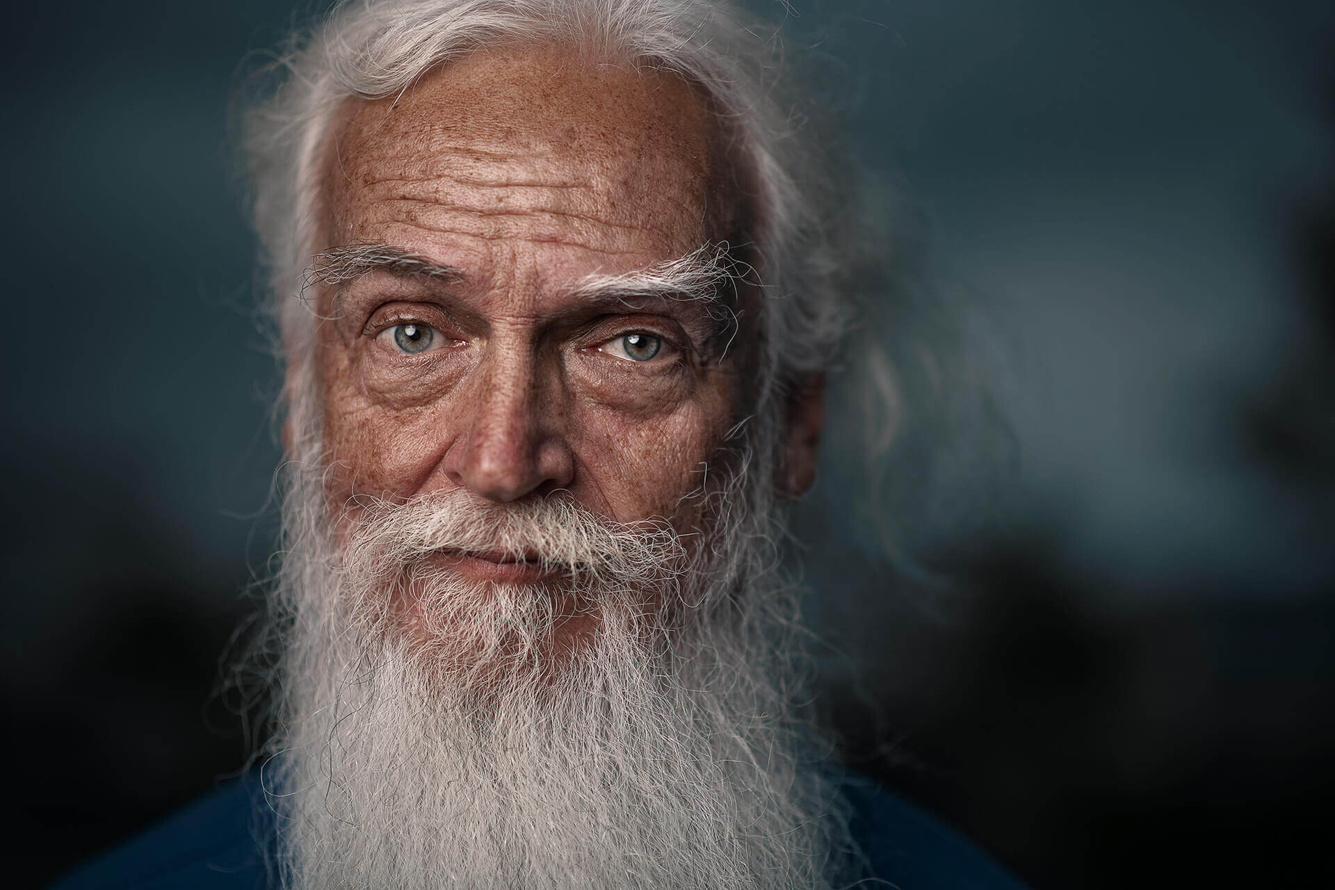 Close portrait of an older man with a white beard and dramatic facial lighting.